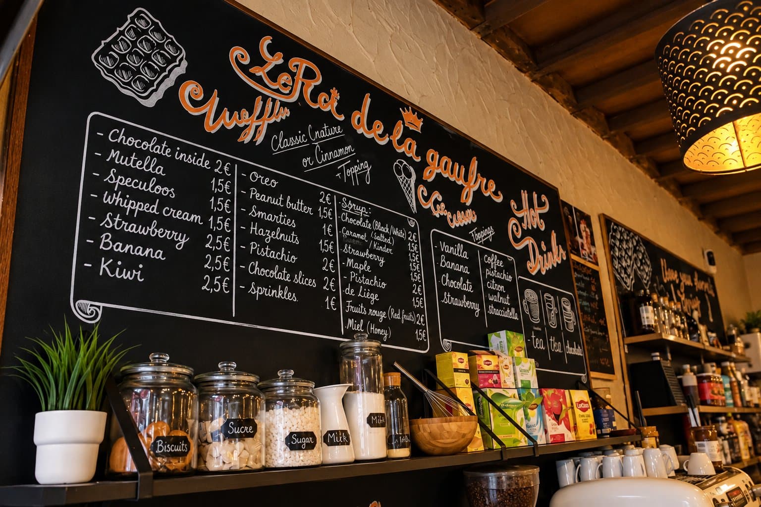 The handwritten chalkboard menu on the wall at Le Roi de la Gaufre, with toppings, syrups and hot drinks